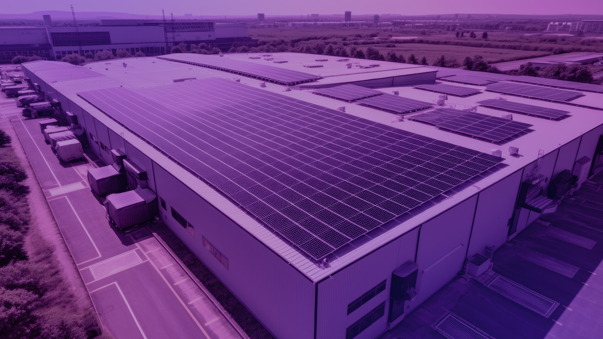 Große Industriehalle mit zahlreichen Solarzellen auf dem Dach, aufgenommen aus der Vogelperspektive. Auf dem Gelände stehen LKWs und Container. Im Hintergrund sind Felder, Straßen und weitere Gebäude sichtbar. Photovoltaik auf Gewerbedächern – Effizienz für Unternehmen nutzen